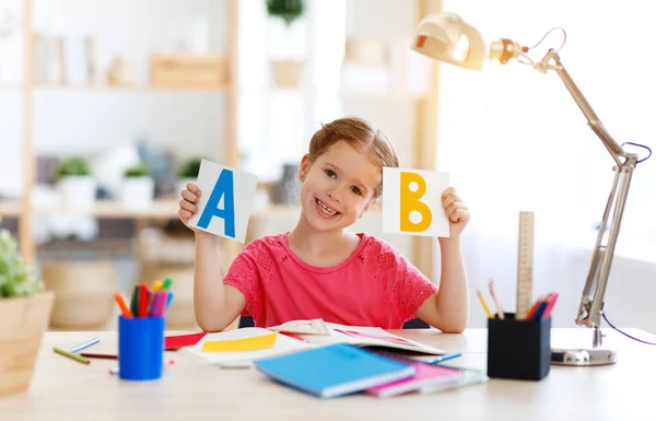 Divertida niña haciendo tareas de escritura y lectura en hom —  Fotos de Stock