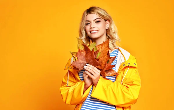 Счастливая эмоциональная девушка с осенними листьями на раскрашенном желтом триколоре — стоковое фото
