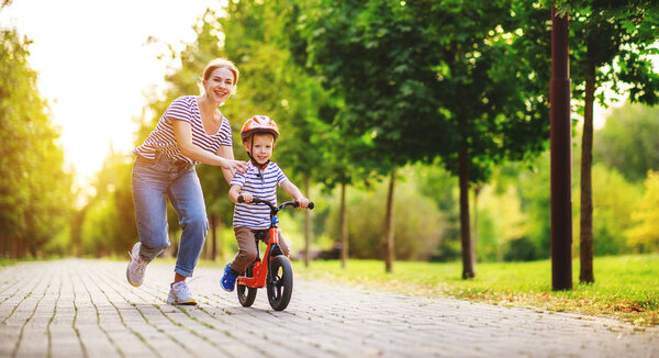 счастливая семья мать учит ребенка сын ездить на велосипеде в парке

