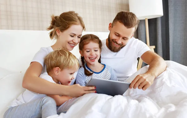Familia feliz riendo con la tableta de ordenador en la cama en casa. reloj — Foto de Stock