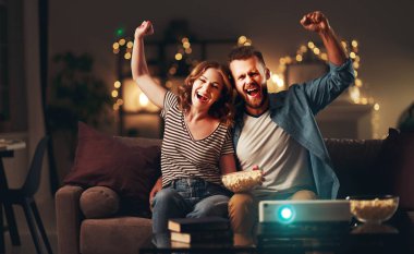 Evde televizyon projektörü izleyen aile çifti