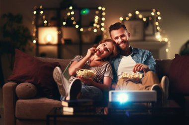 Evde televizyon projektörü izleyen aile çifti