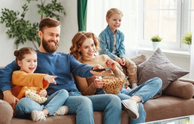 Mutlu, genç ebeveynler ve şirin çocuklar evdeki kanepede oturup patlamış mısır yerken ve hafta sonunun tadını çıkarırken komik filmler izliyorlar.