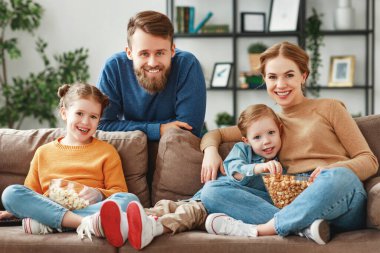 Mutlu, genç ebeveynler ve şirin çocuklar evdeki kanepede oturup patlamış mısır yerken ve hafta sonunun tadını çıkarırken komik filmler izliyorlar.
