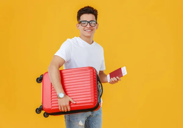Ethnic young man with luggage smiling and looking at camera on yellow backdrop before summer vacatio