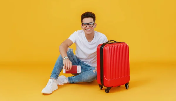 Ethnic young man with luggage smiling and looking at camera on yellow backdrop before summer vacatio