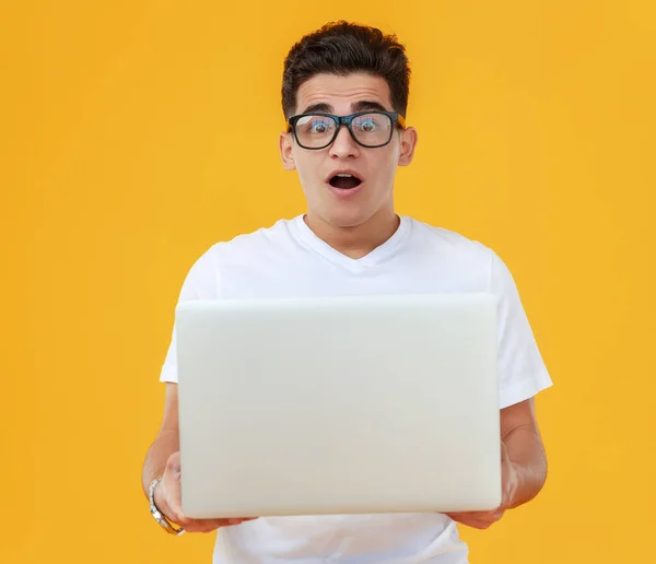 白いTシャツと眼鏡の驚くべき民族の男は ノートパソコンの画面に焦点を当てます黄色の背景に対して口を開けて — ストック写真