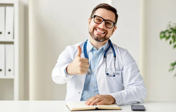 Happy male doctor in uniform and glasses smiling and gesticulating while speaking with patient through video chat ap