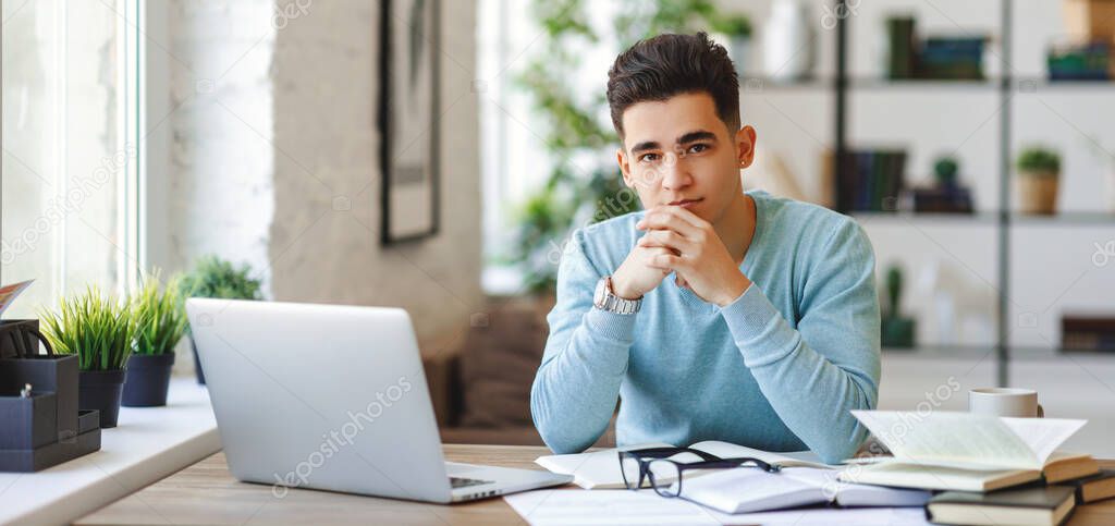 Ethnic young man   sitting at table with laptop and working on remote project at hom