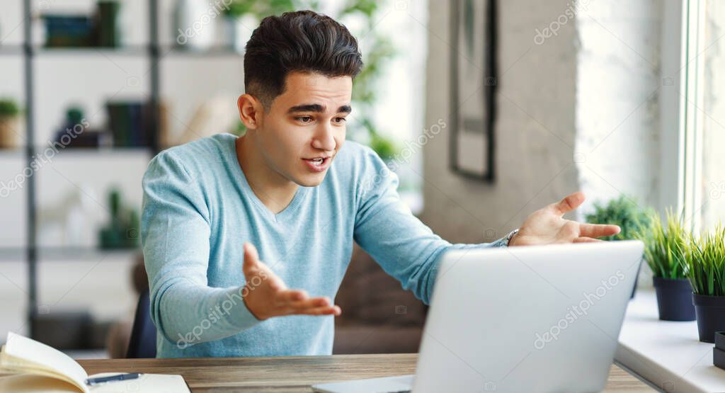 Frustrated ethnic man in glasses making mistake in project and gesticulating while sitting at table and working remotely from hom