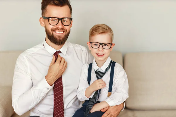 ソファの上で同じような服装で彼の若い息子と一緒に座っていると笑顔でカメラを見て — ストック写真