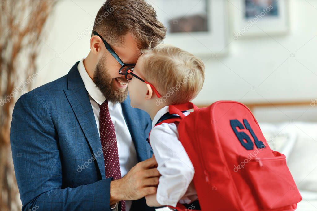 Side view of cheerful dad in formal outfit giving support to delighted kid with schoolbag while preparing for school at hom