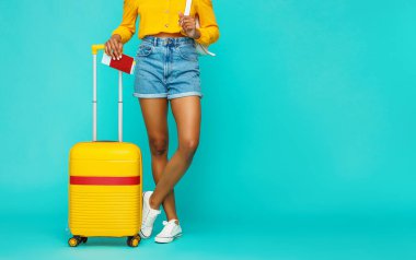 Yaz seyahati konsepti. Bronzlaşmış kadın bacakları şort, pasaport, bilet ve sarı bavul ile parlak mavi bir sırt grubunda