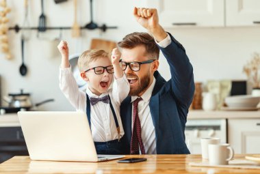 Resmi kıyafetleri ve gözlükleriyle genç bir girişimci dizüstü bilgisayara bakıyor ve modern apartman dairesinde uzaktan çalışırken başarılı bir anlaşmayı kutluyor.