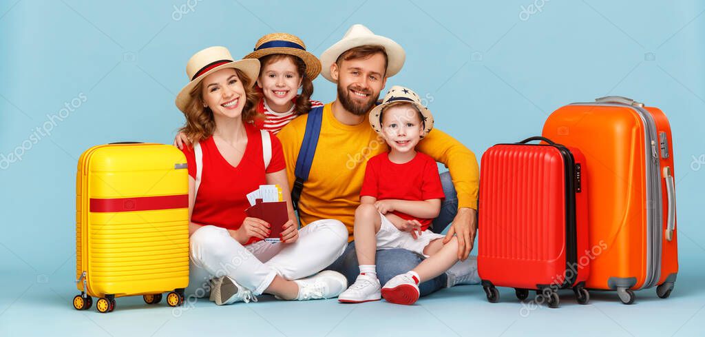 Full body happy parents and children with luggage, passports and tickets smiling and looking at camera against blue backdro
