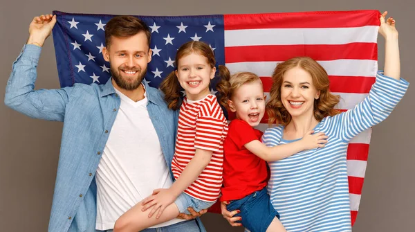 灰色の背景に対する独立記念日を祝いながら アメリカの国旗と明るい子供たちが抱き合ってカメラを見ている幸せな両親 — ストック写真