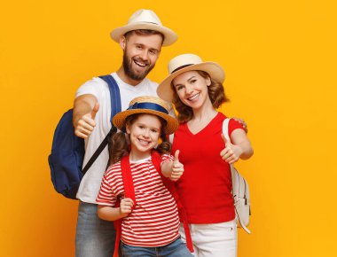 Sırt çantalı, gülümseyen ve kameraya bakan olumlu anne-baba ve kızı yaz tatilinde sarı arka grubuna karşı.