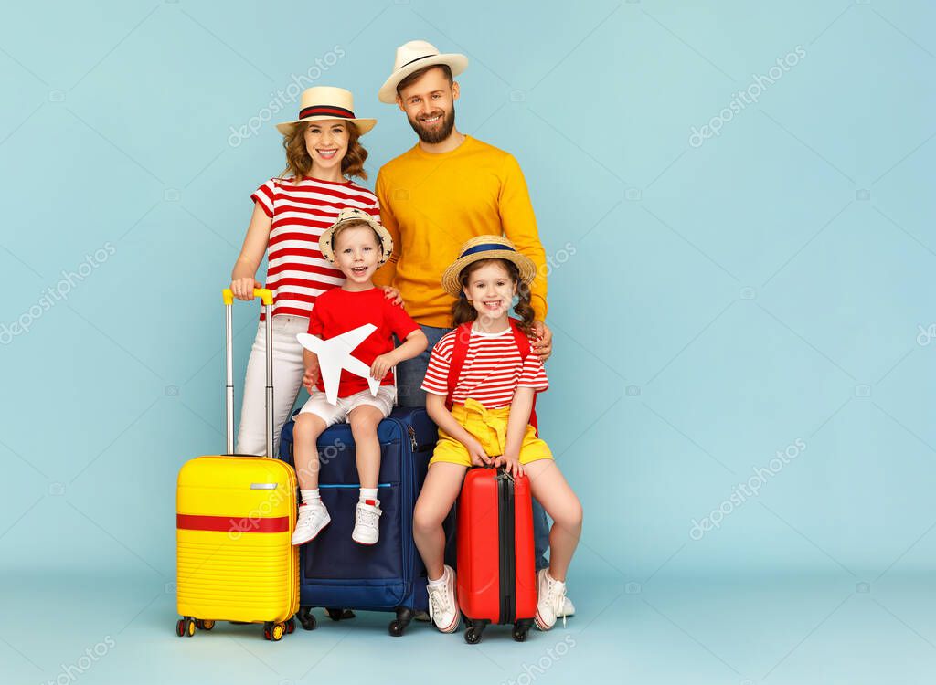 Full body happy family parents and children with luggage smiling and looking at camera against blue backdro