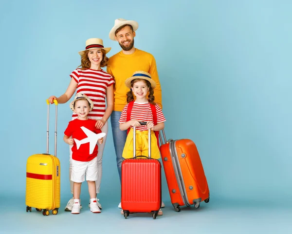 Full body happy parents and kids with luggage and toy plane smiling and looking at camera while being ready for summer vacation against blue backdro