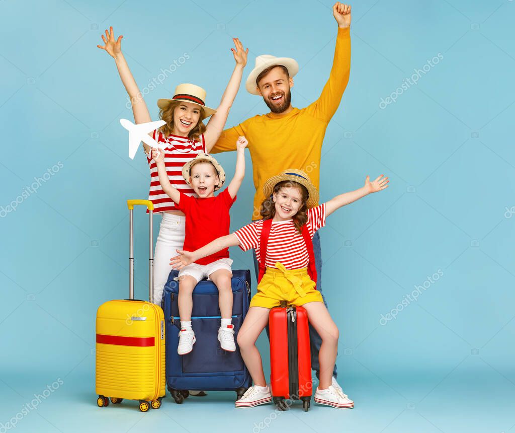 Full body happy family parents and children with arms raised with luggage smiling are glad of the upcoming summer trip against blue backdro