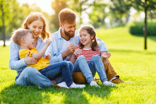 明るい夏の日に緑の草の上に座っている間 陽気な両親は子供たちと笑顔で遊んでいます — ストック写真