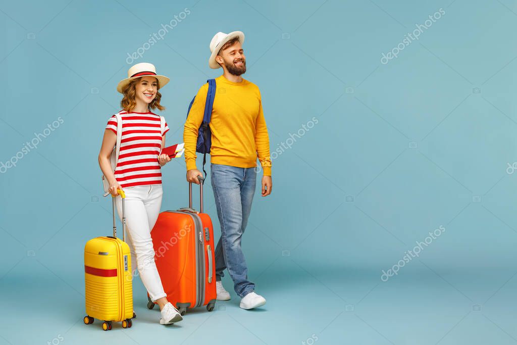 Full body happy couple cheerful bearded man     smiling girlfriend with luggage and tickets during summer vacation against blue backdro