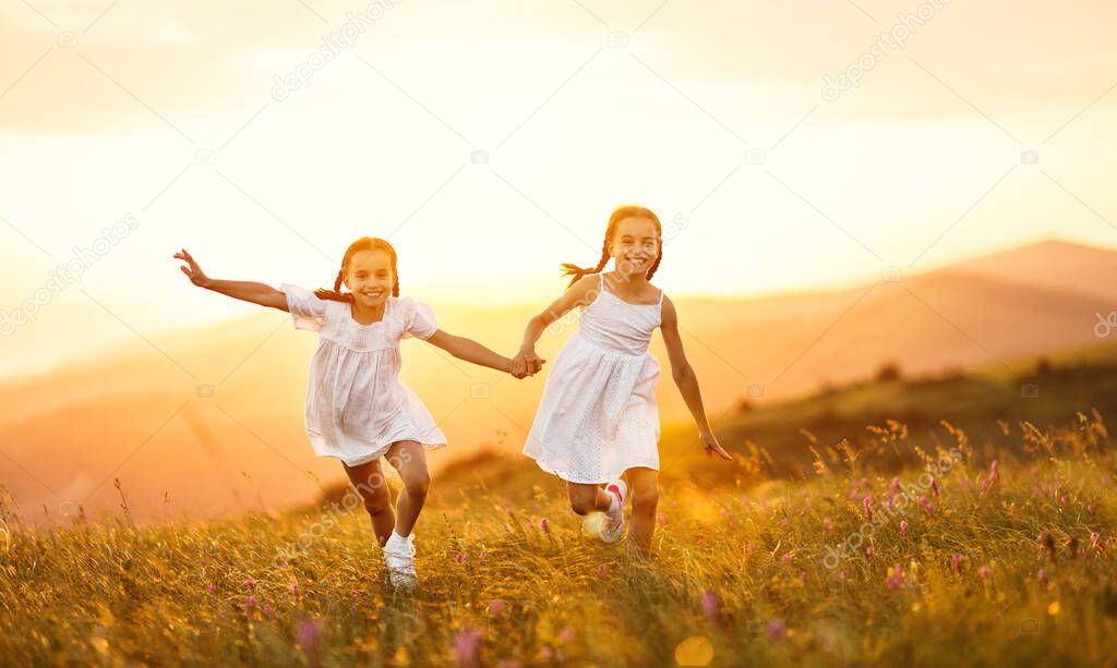 happy children sisters twin girls in white dresses run at sunset in nature in summe
