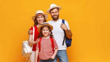 Sırt çantalı, gülümseyen ve kameraya bakan olumlu anne-baba ve kızı yaz tatilinde sarı arka grubuna karşı.