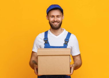 Mutlu sakallı teslimatçı kameraya gülümsüyor ve sarı gruplara karşı çalışırken bir paket taşıyor.
