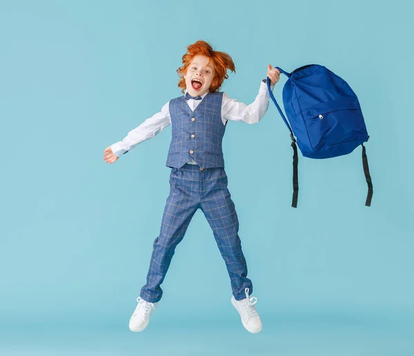 全身喜びました男の子で学校制服叫びと跳躍でバックパックに対して青Backdro — ストック写真