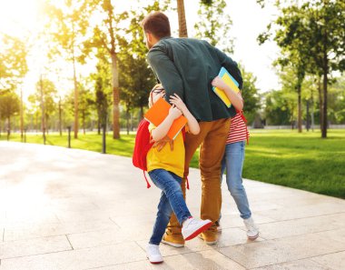 Okuldan sonra çocuklarla tanışırken notlarla neşeli oğlan ve kızı kucaklayan bir adam.