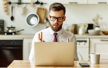 Resmi kıyafetli, ciddi bir genç adam evde vakit geçirirken bilgisayardan iş ortağıyla iletişim kuruyor.