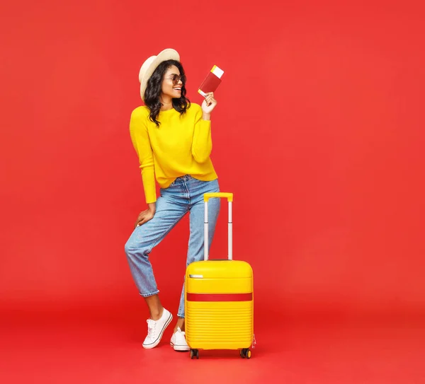 在暑假期间 穿着护照 头戴罚单 满身时髦的女人拿着行李对着红色背风站在镜头前微笑 — 图库照片