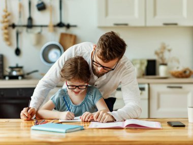 Küçük kızın yanında oturan ve ev ödevlerine yardım ederken zor görevleri açıklayan odaklanmış genç adam.