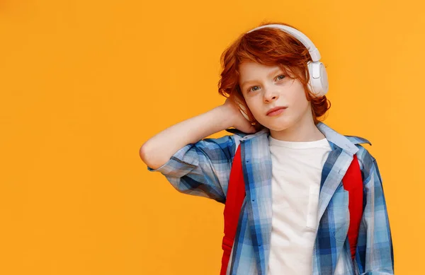 小学生の後の音楽を聞きながらヘッドフォンを調整チェックシャツのジンジャー男の子黄色の背景に対する研究 — ストック写真