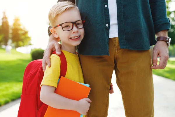 Счастливый Смеющийся Ребенок Маленький Мальчик Школьным Рюкзаком Книгами Обнимает Ногу — стоковое фото