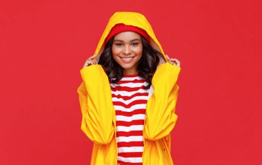 Sarı yağmurluklu, yağmurluklu, yağmurlu bir sonbahar gününde gülümseyen ve kameraya bakan hoş bir kadın.