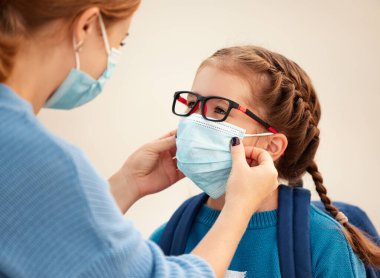 Coronavirus covid-19 ve viral enfeksiyonları önleme kavramı. Anne okuldan önce küçük kız öğrenci için tıbbi maske takıyor.