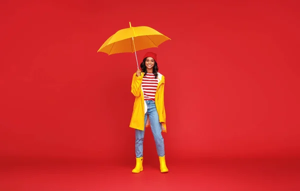 フル長いです楽観的な民族の女性とともに傘笑顔と雨の秋の日にカメラを見て背景色赤 — ストック写真