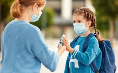 Coronavirus pandemi sırasında okula gitmeden önce küçük kızına dezenfektan şişesi verirken dikkatli ol.