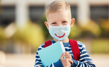 İyimser, birinci sınıf öğrencisi, günlük kıyafetleri ve gözlükleriyle koruyucu bir maske takıyor, elinde telif defterleri ve bulanık şehir grubuna karşı kameraya bakıyor.