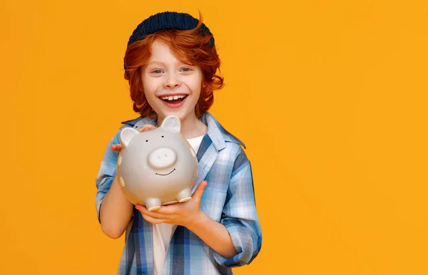 穿着休闲装的积极乐观的男孩笑着 把钱存到储蓄罐里 防止黄色的背影 — 图库照片