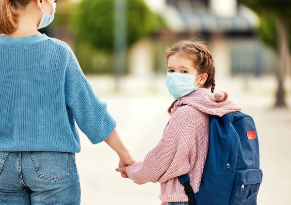 Gündelik giysiler ve sağlık maskesi takmış, tanınmayan bir annenin el ele tutuşup şehir stree 'sinde yürürken görüntüsü.