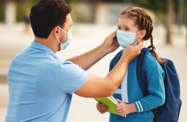 Tanınmayan baba, Coronavirus pandemi sırasında okula hazırlanırken neşeli okul kızının yüzüne tıbbi maske takıyor.