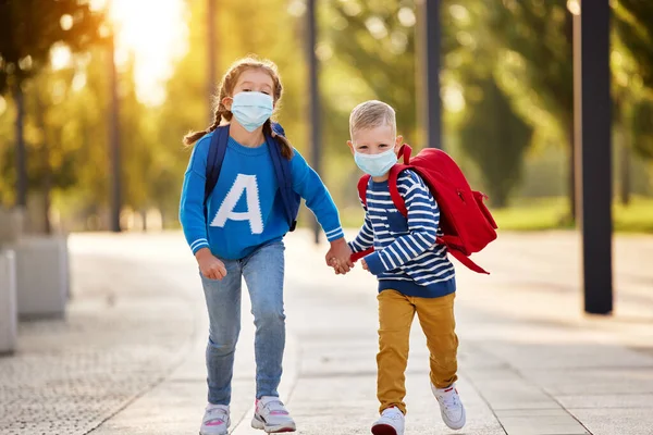 喜形于色的妹妹和弟弟 身穿休闲装 戴着防护面具 手拿背包 一起跑到公园里 准备上学读书 — 图库照片