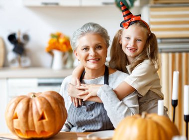 Neşeli kız yaşlı kadına arkadan sarılıyor ve kameraya gülümsüyor. Cadılar Bayramı kutlamaları için balkabağından balkabağına balkabağı oyuyor.