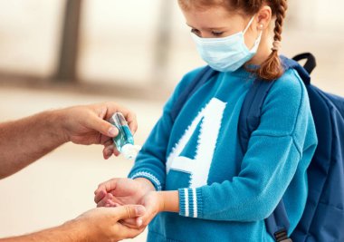 Coronavirus pandemi sırasında okula giden küçük kızın ellerine antiseptik döken isimsiz bir adam.