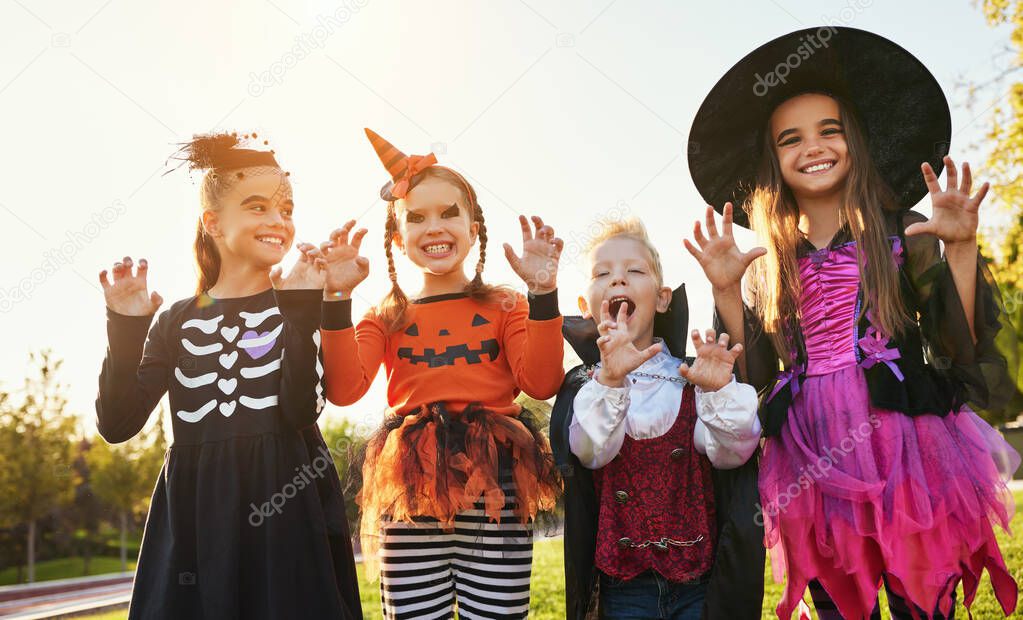 Group of kids in Halloween costumes gesticulating and making scary faces against cloudless sky in par