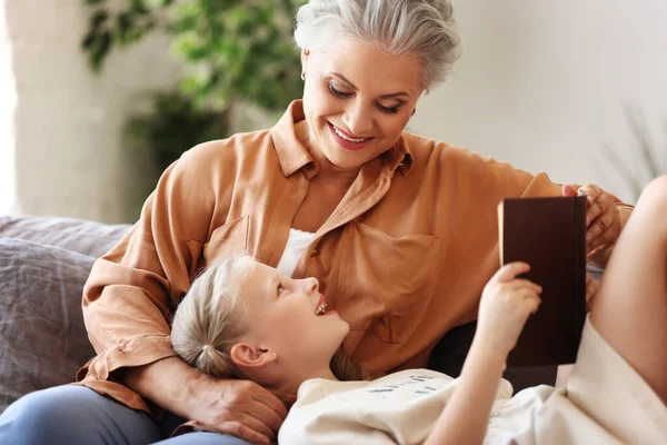 Feliz Anciana Niña Sonriendo Mirándose Mientras Están Sentadas Sofá Leyendo — Foto de Stock