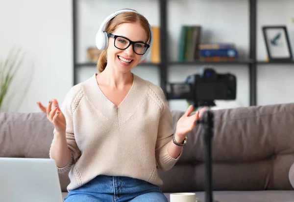 快乐的成年女性博主 戴着耳机和眼镜 一边说着笑话 一边笑着坐在沙发上 记录着视频 — 图库照片
